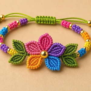 May include: A macrame bracelet featuring a central flower motif with pink, purple, orange, and blue petals, flanked by green leaves. The band consists of colorful knotted cord segments in pink, purple, blue, and yellow, accented with small gold beads.