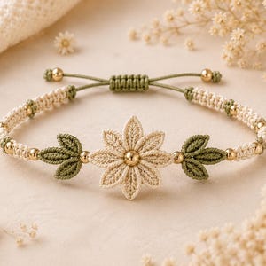 May include: A macrame bracelet featuring a central cream-coloured flower motif with a gold bead centre, flanked by two green leaf-shaped accents. The band is crafted from cream and green cord, interspersed with small gold beads and an adjustable closure.
