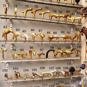 K&ouml;nnte beinhalten: Eine Sammlung antiker T&uuml;rgriffe und Kn&ouml;pfe aus Messing, jeweils mit einzigartigem Design. Die Hardware wird auf mehreren Regalen pr&auml;sentiert und zeigt verschiedene Formen und Stile, darunter verzierte und schlichte Designs. Das Bild ist ein Katalog f&uuml;r Vintage-T&uuml;rbeschl&auml;ge.