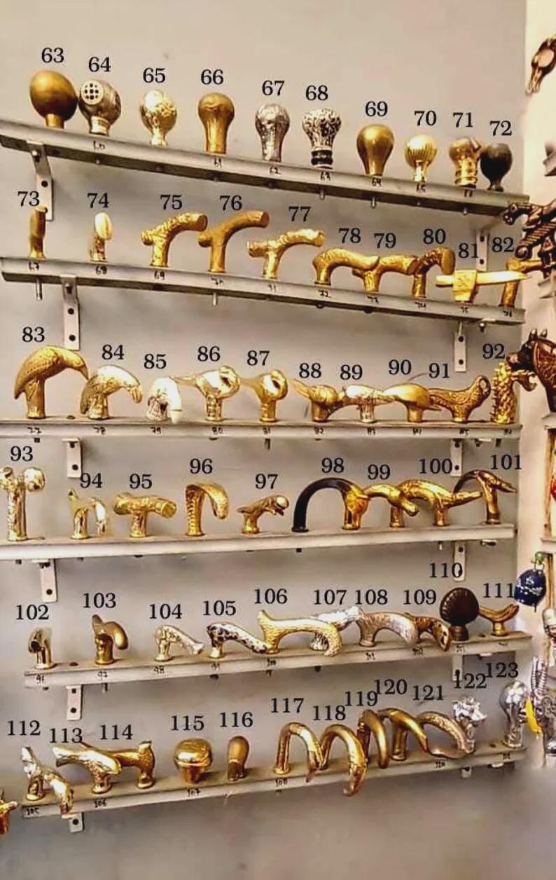 K&ouml;nnte beinhalten: Eine Sammlung antiker T&uuml;rgriffe und Kn&ouml;pfe aus Messing, jeweils mit einzigartigem Design. Die Hardware wird auf mehreren Regalen pr&auml;sentiert und zeigt verschiedene Formen und Stile, darunter verzierte und schlichte Designs. Das Bild ist ein Katalog f&uuml;r Vintage-T&uuml;rbeschl&auml;ge.