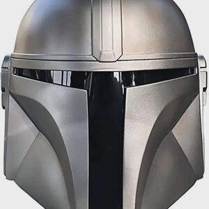May include: A metallic silver Mandalorian helmet with a distinctive T-shaped visor and a rounded top. The helmet features angular cheek plates and a central vertical ridge, showcasing a sleek, futuristic design. The helmet is a replica of the one worn by the Mandalorian.