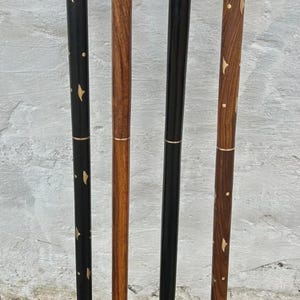 K&ouml;nnte beinhalten: Vier Holzspazierst&ouml;cke. Zwei sind schwarz mit goldenen Akzenten, und zwei sind braun mit Holzmaserungsmustern. Jeder Stock hat eine Metallspitze und ein goldenes Band in der N&auml;he von oben und unten.