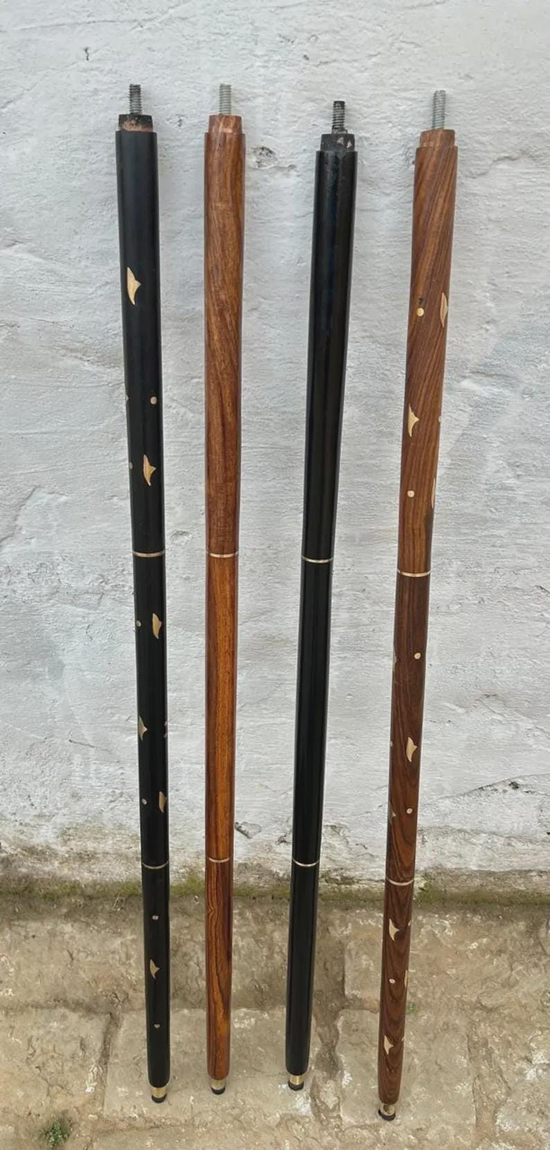 K&ouml;nnte beinhalten: Vier Holzspazierst&ouml;cke. Zwei sind schwarz mit goldenen Akzenten, und zwei sind braun mit Holzmaserungsmustern. Jeder Stock hat eine Metallspitze und ein goldenes Band in der N&auml;he von oben und unten.