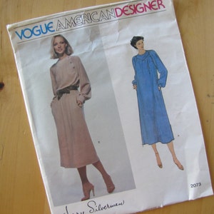 May include: Vogue American Designer sewing pattern number 2073 by Jerry Silverman. The pattern features two dress designs, one in a light brown color and the other in a light blue color.