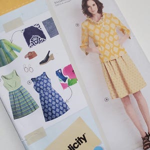 May include: A sewing pattern package from Lisette and Simplicity. The package features a woman in a yellow outfit, with a dress and jacket design. The package also shows dress and jacket design options.
