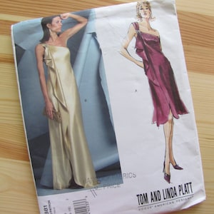 May include: A sewing pattern for a dress with a one-shoulder design. The pattern is from Vogue American Designer, Tom and Linda Platt, and is for sizes 12-14-16. The pattern shows two different styles of the dress, one in a gold color and the other in a burgundy color.