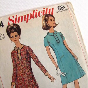 Peut inclure: Patron de couture Simplicity numéro 65c, présentant deux robes. Une robe est une robe chemise bleue avec un col et des manches courtes. L'autre robe est une robe à imprimé floral rouge et marron avec un col et des manches longues. Le texte "Simplicity" est imprimé en rouge et blanc sur le patron.