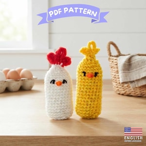 May include: A PDF pattern featuring two crocheted figures: a white chicken with a red comb and orange beak, and a yellow chick with an orange beak. Both have black embroidered eyes. A banner at the top reads PDF PATTERN and a flag icon says ENGLISH.