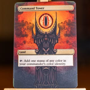 May include: A Magic: The Gathering card titled "Command Tower." The card features a dark, ominous tower design with a fiery orange and red sky background. The text "Land" and card text are visible.