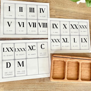 May include: A set of flashcards with Roman numerals from I to M, with corresponding Arabic numerals and words. A wooden tray with three compartments is also visible.