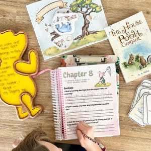 May include: A spiral-bound workbook titled Chapter 8 In Which Piglet Does A Very Grand Thing, a yellow wooden Winnie the Pooh shaped board with handwritten text, a book titled The House at Pooh Corner, and illustrated character cutouts.