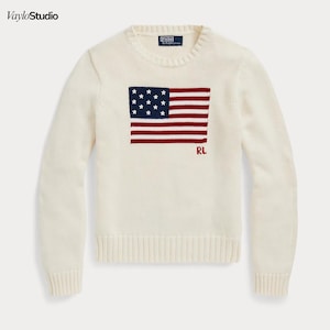 May include: Cream-colored sweater featuring a crew neck and long sleeves. The front displays a graphic of the American flag in red, white, and blue, with the initials "RL" in red. The sweater is made of a soft, knitted material.