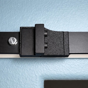 May include: Close-up of a black metal sliding door hardware system. The hardware includes a black track, a textured bracket, and a bolt. The background is a light blue wall.