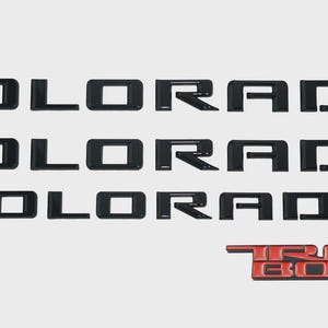 May include: Black "COLORADO" lettering and a red "TRAIL BOSS" emblem. The word "COLORADO" is displayed three times in a stacked arrangement. The "TRAIL BOSS" emblem is in red with a black outline.