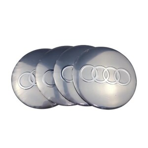 May include: Four silver hubcaps with the Audi logo, featuring four interlocking rings. The hubcaps are arranged in a slightly overlapping pattern, with a reflective surface and a bright, clean appearance.
