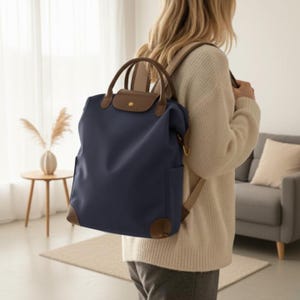 Puede incluir: Mochila azul marino con detalles en cuero marrón. La bolsa tiene un cierre de solapa y un asa superior. Las esquinas y la solapa son de cuero marrón. La mochila se lleva como mochila.