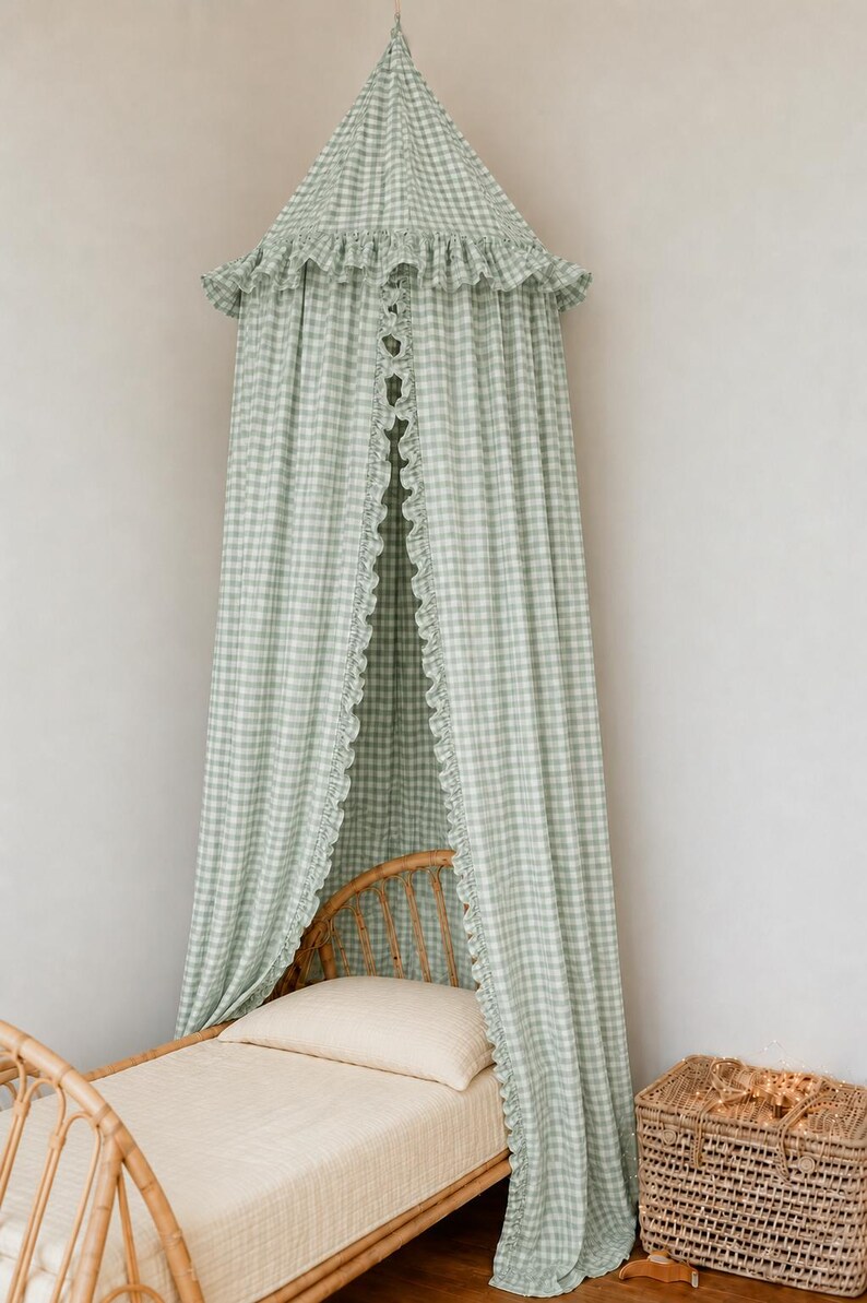 May include: A sage green and white gingham fabric canopy featuring a conical top with a ruffled edge and long, flowing panels that drape downward. The canopy includes a vertical ruffled trim along the front opening, creating a soft, layered look.