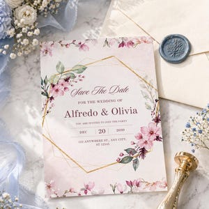 Puede incluir: Una invitación de boda con el texto "Save The Date" y los nombres "Alfredo & Olivia". La invitación está decorada con detalles florales rosas y un marco geométrico dorado. También se ve un sello de cera azul y un sello de lacre dorado.