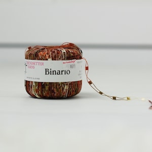 May include: A ball of yarn in shades of brown, orange, and green. The label says "Trendsetter Yarns" and "Binario". A tag with a price is attached to the yarn.