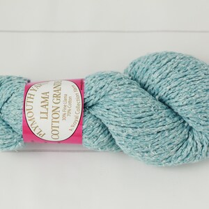 May include: A skein of Plymouth Yarn Llama Cotton Grande in a light teal color. The yarn is a blend of fine llama and cotton, with a pink and white label wrapped around the center. The label reads "Llama Cotton Grande".