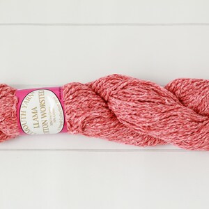 May include: A skein of red and white speckled yarn, labeled "South Yarn Llama Cotton Worsted." The yarn is tightly wound and has a soft, textured appearance. Ideal for knitting and crochet projects.