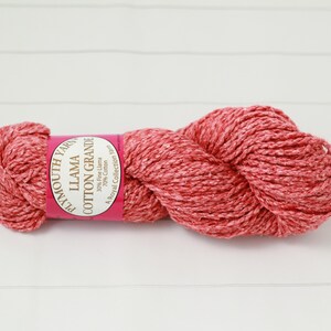 May include: A skein of Plymouth Yarn Llama Cotton Grande in a coral and white color. The yarn is tightly wound and has a textured appearance. The label reads "Llama Cotton Grande" and lists the fiber content. Ideal for knitting and crochet projects.