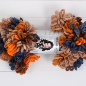 May include: Two balls of yarn in shades of brown, orange, and blue. The yarn is fluffy and textured. The yarn is labeled "Dolce Vita".