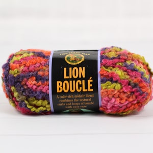 May include: A colorful ball of Lion Bouclé yarn, featuring a mix of purple, pink, orange, and green hues. The yarn is a mohair blend with a textured, looped appearance. The label reads "Lion Bouclé".