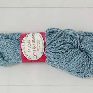 May include: A skein of Plymouth Yarn Llama Cotton Grande in a light blue color. The yarn is a blend of llama and cotton, with a label that reads "Llama Cotton Grande". The yarn is a Royal Collection Yarn.