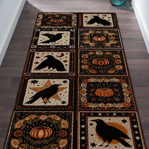 May include: A rectangular runner rug featuring a grid of square panels with alternating illustrations of black crows, orange pumpkins, stars, and floral wreaths. The color palette includes deep black, burnt orange, cream, and brown tones.