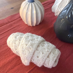 Könnte beinhalten: Ein gerolltes, cremefarbenes, gehäkeltes Objekt, möglicherweise ein Waschlappen oder kleines Handtuch, liegt auf einer roten Oberfläche. Dekorative Kerzenhalter mit blauen und weißen Akzenten deuten auf ein Wohnkulturthema hin.