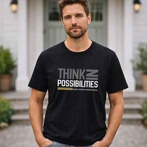 Könnte beinhalten: Schwarzes T-Shirt mit Rundhalsausschnitt und den Worten "THINK POSSIBILITIES" in Grau und Weiß, mit einer goldenen horizontalen Linie. Der Text "open minds creates future" steht darunter. Das T-Shirt wird von einer Person getragen.
