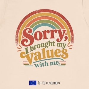 Puede incluir: Una camiseta de color crema con un gráfico desgastado de un arcoíris multicolor sobre el texto "Sorry, I brought my values with me." El diseño utiliza tonos rojos, naranjas, amarillos, verdes y azules. Se incluye un pequeño icono de la bandera de la UE.