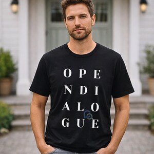 Könnte beinhalten: Schwarzes T-Shirt mit Rundhalsausschnitt und dem weißen Aufdruck "OPEN DIALOGUE" in Großbuchstaben. Das Shirt besteht aus einem weichen Material und wird von einer Person getragen.