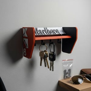 Könnte beinhalten: Ein an der Wand befestigter Schlüsselhalter in Form eines Formel-1-Flügels mit orangefarbenen und schwarzen Akzenten. Der Schlüsselhalter trägt den Schriftzug "Marlboro", und mehrere Schlüssel hängen an den Haken.