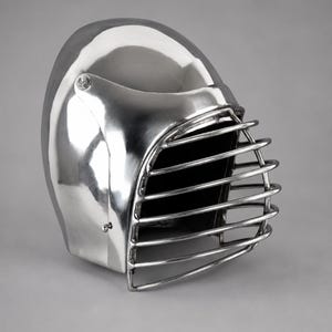 May include: A polished silver-colored metal helmet featuring a smooth, rounded dome and a protective cage-style face guard. The front of the helmet is open, covered by horizontal metal bars that are secured to the sides with visible hardware.