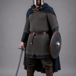 Peut inclure: Un casque en métal argenté à sommet pointu, une cotte de mailles, une cape bleu foncé avec une broche circulaire, une ceinture en cuir marron, un pantalon sombre, des bottes en cuir marron, un bouclier rond avec un umbo et une longue épée en acier.