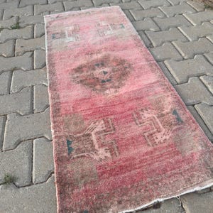 Puede incluir: Una alfombra rectangular tipo pasillero con una paleta de colores rosa y marrón descoloridos. La alfombra presenta un motivo de medallón central rodeado de patrones geométricos y formas estilizadas en tonos apagados y textura desgastada.