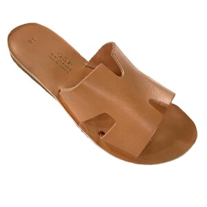 Peut inclure: Une paire de sandales en cuir marron clair. Les sandales ont un design simple avec une bride sur le dessus et une semelle plate. Les sandales sont de taille 38 et sont fabriquées en Grèce.