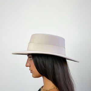 May include: A light beige fedora hat with a wide brim and a matching band. The hat is made of a soft material and has a classic, timeless design. The hat's brim measures approximately 3 inches (7.6 cm) wide.