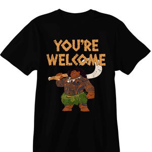 May include: Black t-shirt featuring a cartoon illustration of a Polynesian figure holding a weapon. The text "YOU'RE WELCOME" is printed above the character in a distressed, orange font. The character is wearing a leaf skirt.