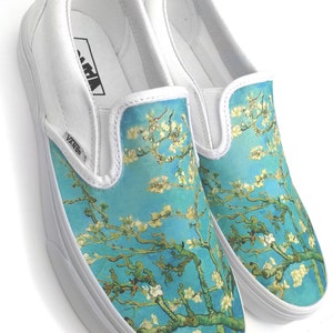 Puede incluir: Zapatillas Vans blancas de deslizamiento con un estampado floral azul y blanco. El estampado presenta una representaci&oacute;n estilizada de una rama de almendro en flor, que recuerda a la obra de arte de Vincent van Gogh.