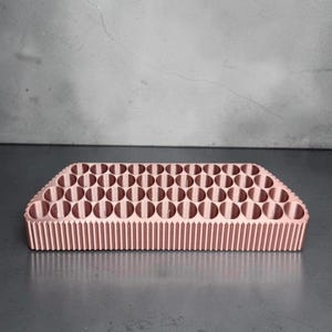 May include: A rose gold colored rectangular organizer tray featuring a grid of numerous circular storage compartments. The exterior sides of the tray are designed with a vertical ribbed texture, providing a structured and uniform appearance.