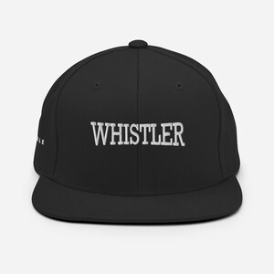 Pode incluir: Boné de beisebol preto com a palavra "WHISTLER" bordada em branco na frente. O boné tem uma aba plana e um ajuste estruturado. A palavra "ALE" é bordada na lateral.