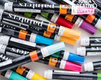 May include: A collection of colorful paint pens with black barrels and white caps. The pens are arranged in a scattered pattern, showcasing various colors like orange, yellow, blue, pink, and purple. The text "painters" is visible on the pens.