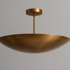 May include: A modern, gold-toned ceiling light fixture. The fixture features a shallow, bowl-shaped shade suspended from a central rod and a circular ceiling mount. The overall design is minimalist and elegant, suitable for various interior styles.