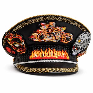 May include: A black military-style cap featuring a central embroidered patch of a skeleton riding a motorcycle engulfed in flames, flanked by two skull patches. The cap is decorated with gold braided trim, a red flame band, and crystal accents.