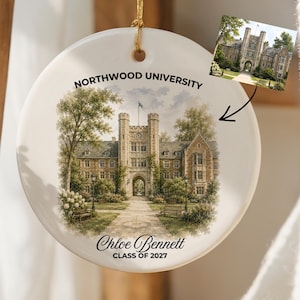 May include: A round white ceramic ornament featuring a printed illustration of a stone university building with a central archway. The text reads Northwood University, Chloe Bennett, and Class of 2027. A gold string is attached for hanging.