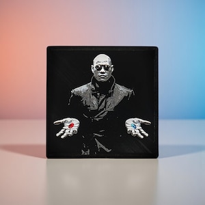 May include: Black square art print depicting a man in a long coat, rendered in grayscale, with outstretched hands. Each hand holds a pill, one red and one blue. The background is black, with a pink and blue gradient.