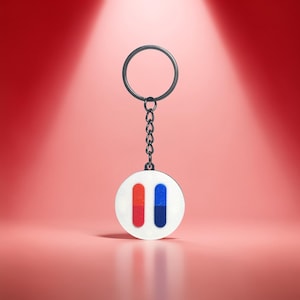 May include: A round white keychain pendant with a red and blue vertical stripe design. The pendant is attached to a silver chain and keyring. The background is a gradient of red and pink.
